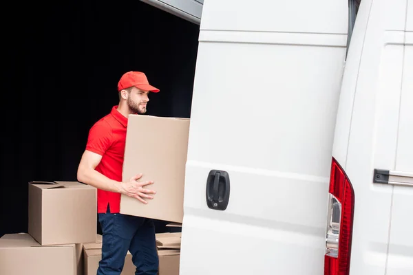 Vista lateral del joven repartidor descargando cajas de cartón de la furgoneta - foto de stock