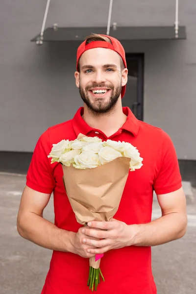 Portrait of cheerful delivery man holding bouquet of roses on street — Stock Photo