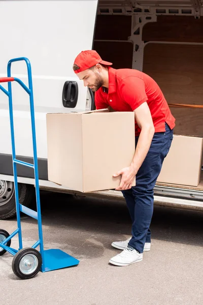 Young delivery man discharging cardboard boxes from van — Stock Photo