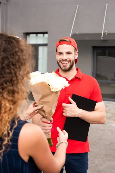 Частковий вид клієнта і усміхнений чоловік доставки з блокнотом і букетом троянд — стокове фото