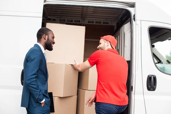 Caucasian delivery man showing cargo to african american client — Stock Photo