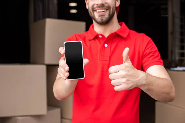Обрізаний знімок веселого чоловіка доставки зі смартфоном, що показує великий палець вгору — стокове фото