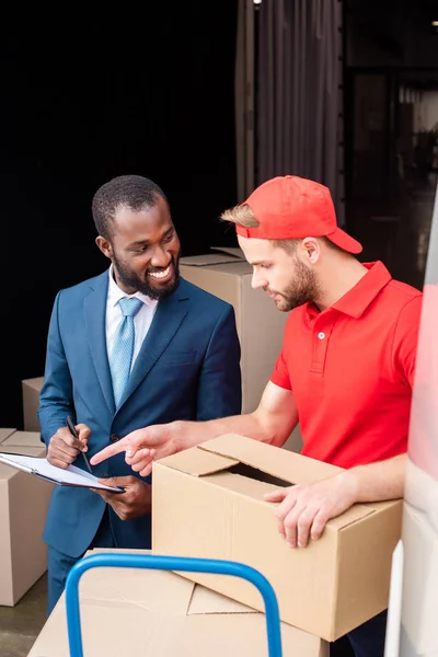 Portrait of multicultural businessman and delivery man discussing order — Stock Photo