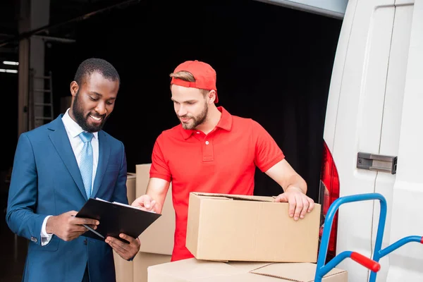 Portrait of multicultural businessman and delivery man discussing order — Stock Photo