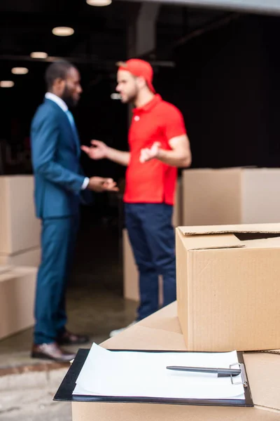 Focus selettivo di uomo d'affari multiculturale e uomo di consegna discutendo ordine — Foto stock