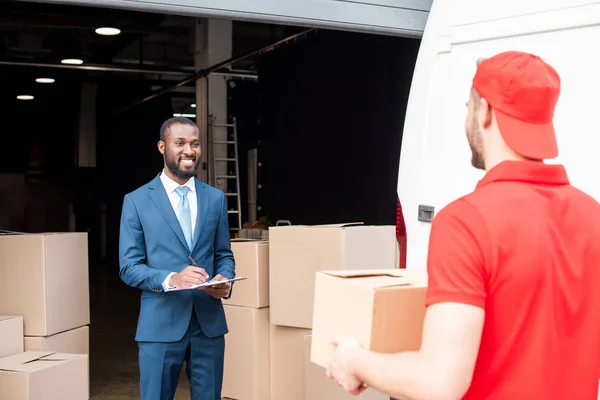 Selective focus of multicultural businessman and delivery man with cargo — Stock Photo