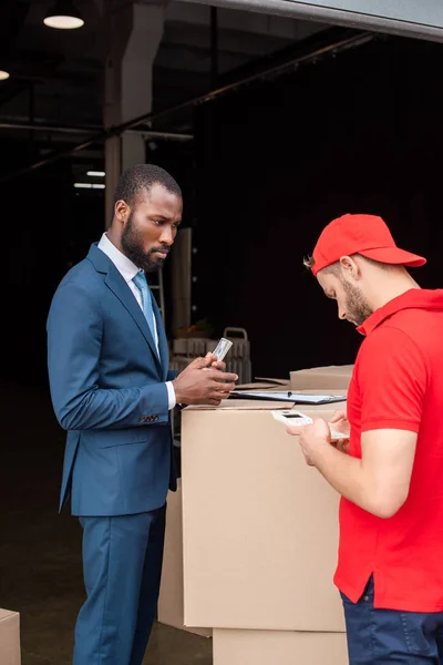 Cliente americano africano com dinheiro e homem de entrega caucasiano com calculadora — Fotografia de Stock