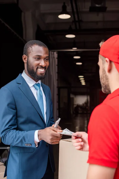 Cliente afroamericano sonriente que paga la entrega con efectivo - foto de stock