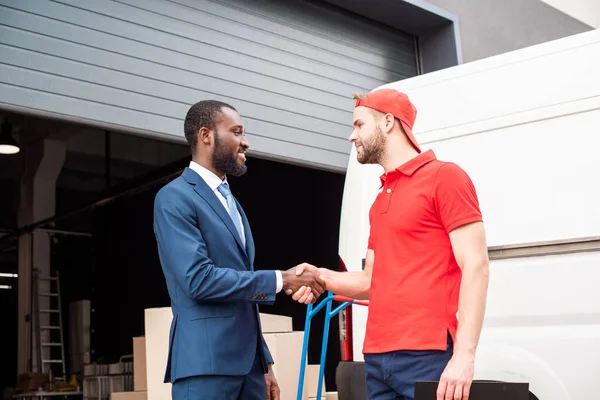 Vue latérale d'un client multiculturel et d'un livreur serrant la main près de van — Photo de stock