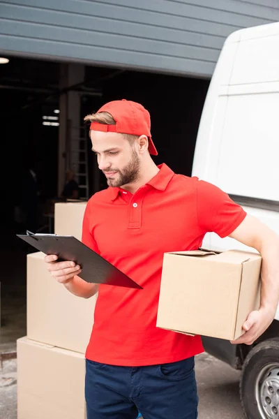 Retrato del joven repartidor con caja de cartón y bloc de notas - foto de stock