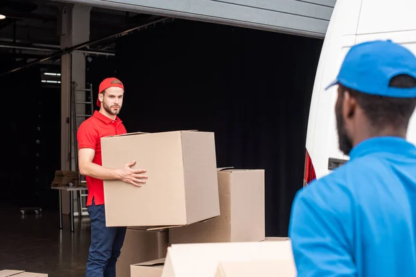 Homens de entrega multicultural em uniforme vermelho e azul com caixas de papelão — Fotografia de Stock