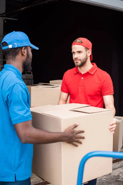 Homens de entrega multicultural em uniforme vermelho e azul com caixas de papelão — Fotografia de Stock