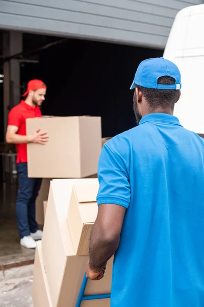 Homens de entrega multiétnicos em uniforme vermelho e azul com caixas de papelão — Fotografia de Stock