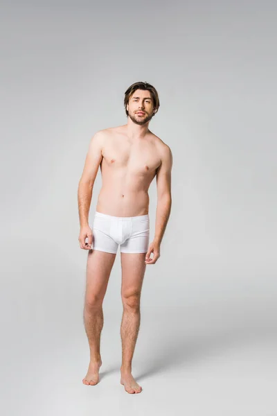 Jeune homme en sous-vêtements blancs posant sur fond gris — Photo de stock