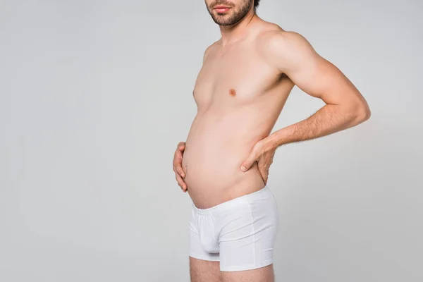 Частичный вид человека в белом нижнем белье с опухшим желудком, изолированным на сером — стоковое фото