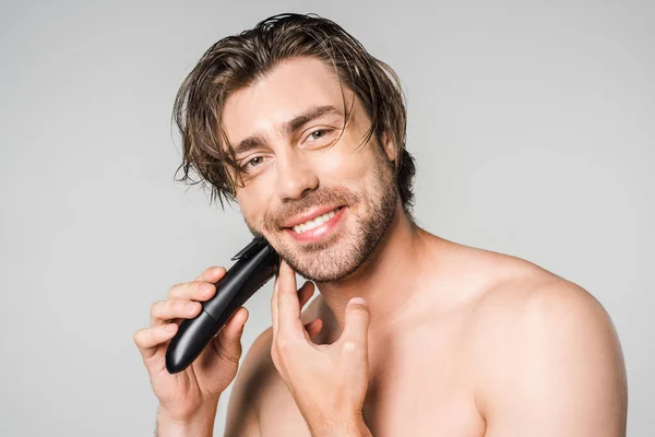 Ritratto di uomo bello sorridente con la barba da barba elettrica clipper isolato su grigio — Foto stock