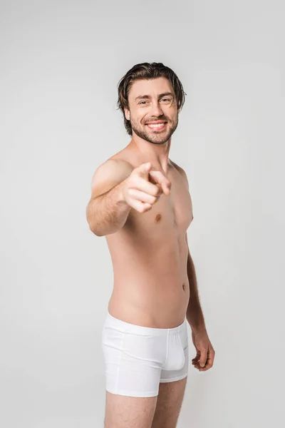 Портрет улыбающегося мужчины в белом нижнем белье, указывающего на камеру, изолированную на сером — стоковое фото