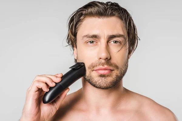 Портрет красивого мужчины с электрическим клиппером, изолированным на сером — стоковое фото