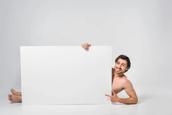 Smiling handsome man pointing at blank banner on grey background — Stock Photo