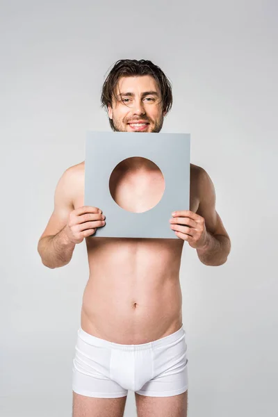 Portrait of young smiling man in underwear holding circle paper figure isolated on grey — Stock Photo