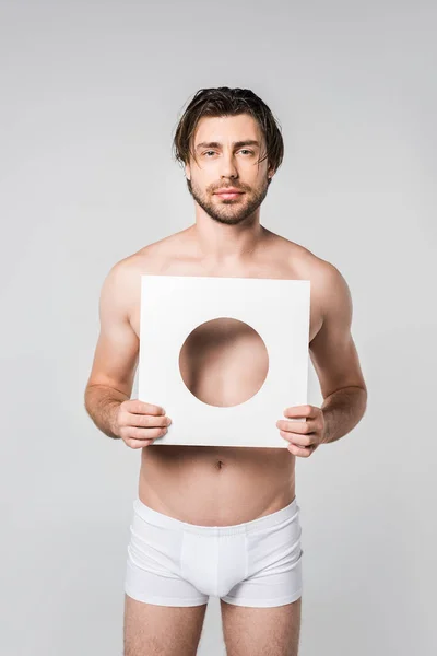 Retrato de un joven en ropa interior sosteniendo la figura de papel círculo aislado en gris - foto de stock