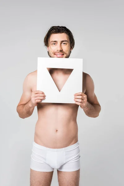 Portrait of young smiling man in underwear holding triangle paper figure isolated on grey — Stock Photo