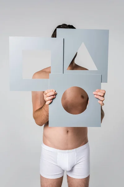 Obscured view of man in underwear holding grey paper figures in hands isolated on grey — Stock Photo