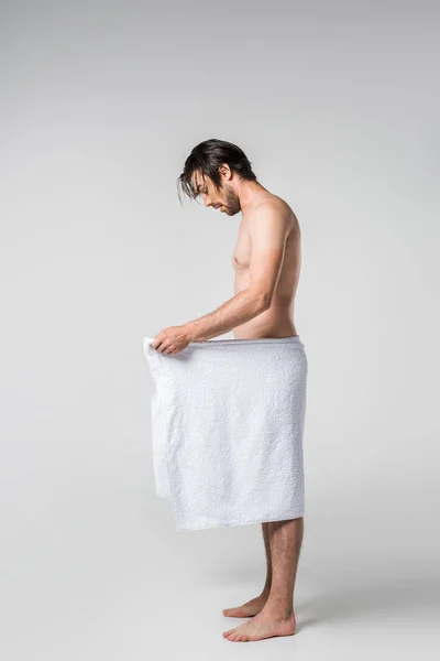 Vista lateral de homem bonito em toalha branca olhando para baixo no fundo cinza — Fotografia de Stock