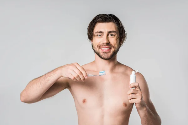 Porträt eines lächelnden, hemdlosen Mannes mit Zahnbürste und Zahnpasta isoliert auf grau — Stockfoto