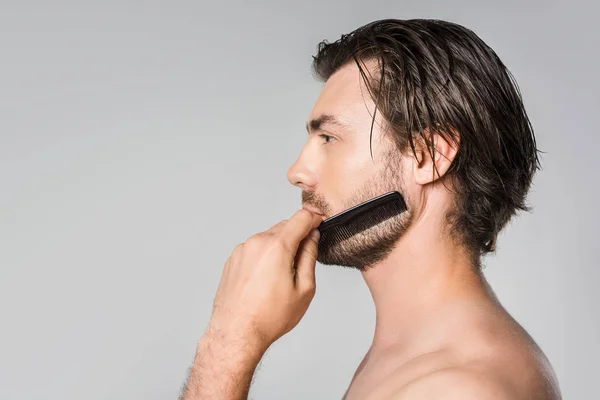 Vista laterale dell'uomo spazzolatura barba con pettine isolato su grigio — Foto stock