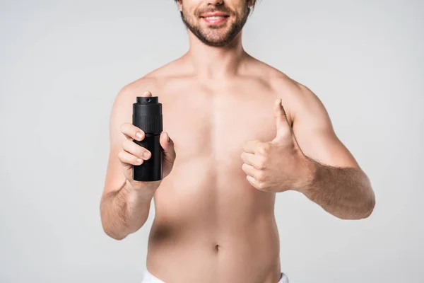 Partial view of smiling man with male deodorant showing thumb up isolated on grey — Stock Photo