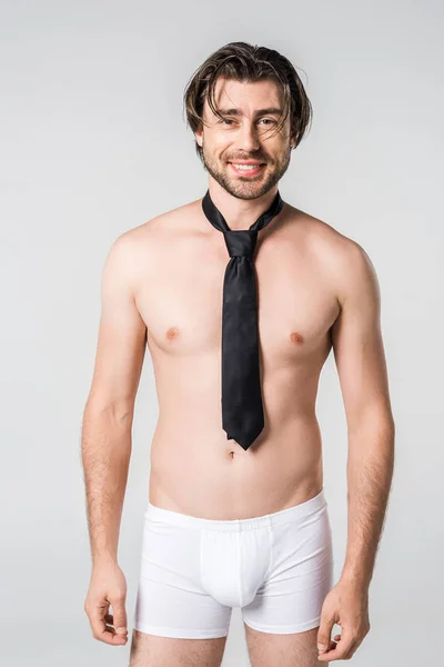 Портрет улыбающегося мужчины в белых трусах с черным галстуком на сером фоне — стоковое фото