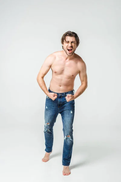 Homem sem camisa emocional em jeans mostrando músculos em pano de fundo cinza — Fotografia de Stock