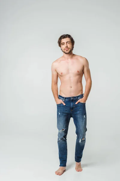 Jovem sem camisa homem em jeans com as mãos nos bolsos posando no fundo cinza — Fotografia de Stock