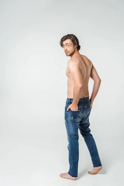 Вид ззаду молодого без сорочки в джинсах на сірому фоні — стокове фото