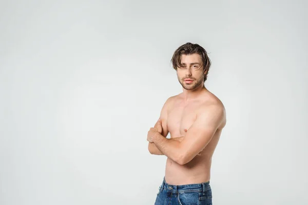 Портрет задумчивого мужчины без рубашки в джинсах, смотрящего на камеру, изолированную на сером — стоковое фото