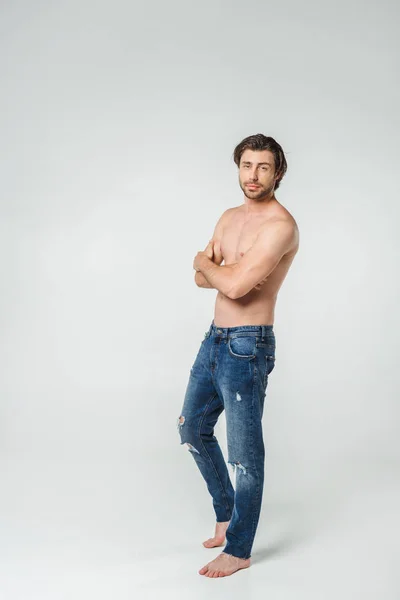 Young shirtless man in jeans with arms crossed looking at camera on grey backdrop — Stock Photo