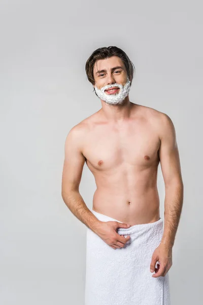 Portrait of shirtless man in towel with shaving foam on face isolated on grey — Stock Photo