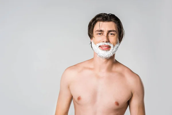 Портрет молодої людини з піною для гоління на обличчі, дивлячись на камеру ізольовано на сірому — стокове фото