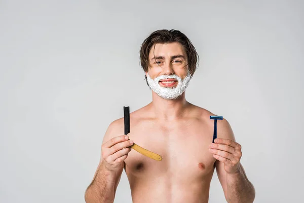 Portrait of smiling man with shaving foam on face holding razors isolated on grey — Stock Photo