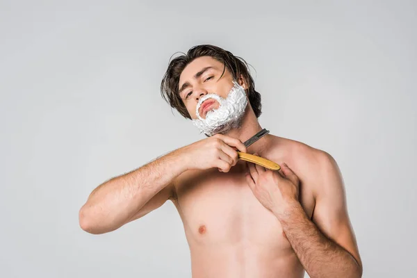 Portrait of shirtless man with foam on face shaving beard isolated on grey — Stock Photo