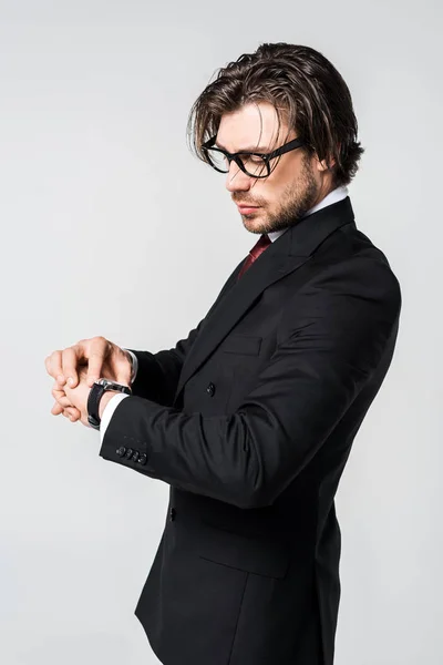 Jeune homme d'affaires en costume élégant et lunettes temps de contrôle isolé sur gris — Photo de stock