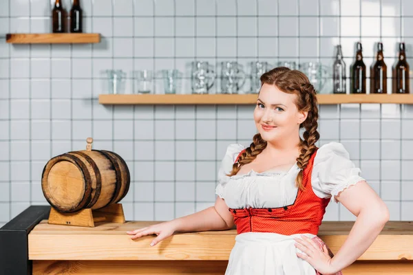 Atraente garçonete oktoberfest em vestido tradicional da Baviera de pé perto bar contador com barril de cerveja — Fotografia de Stock