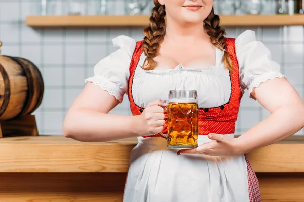 Cropped imageo of oktoberfest bartender in traditional bavarian dress holding mug of light beer near bar counter — Stock Photo
