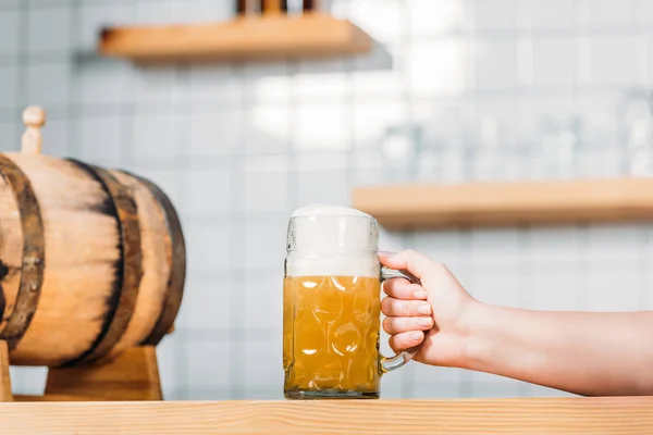 Cropped image of female bartender putting mug of light beer with foam on bar counter with beer barrel — Stock Photo