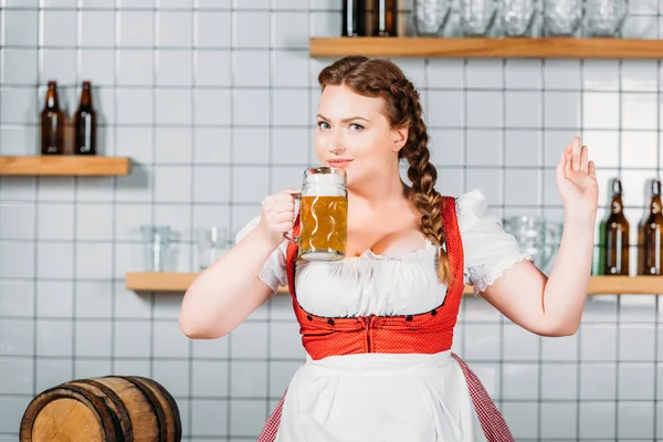 Camarera sonriente oktoberfest en vestido bavariano tradicional beber cerveza ligera cerca del mostrador del bar - foto de stock