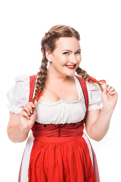 Smiling oktoberfest waitress in traditional bavarian dress holding pigtails isolated on white background — Stock Photo