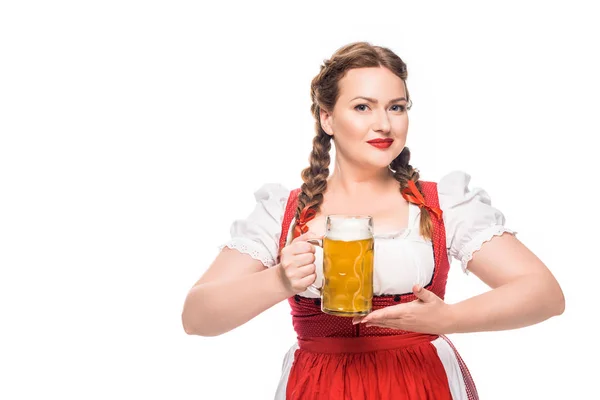 Atractiva camarera oktoberfest en vestido bavariano tradicional sosteniendo taza de cerveza ligera aislada sobre fondo blanco - foto de stock