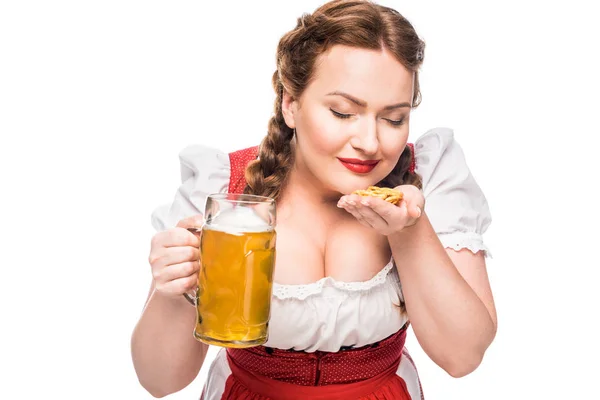 Oktoberfest waitress in traditional german dress with mug of light beer smelling little pretzels isolated on white background — Stock Photo