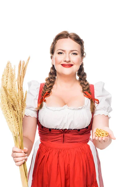 Serveuse oktoberfest en tenue bavaroise traditionnelle montrant de petits bretzels et tenant des épis de blé isolés sur fond blanc — Photo de stock